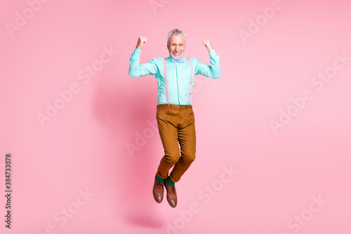 Full length body size photo of smiling granddaddy jumping high gesturing like winner isolated on pink color background
