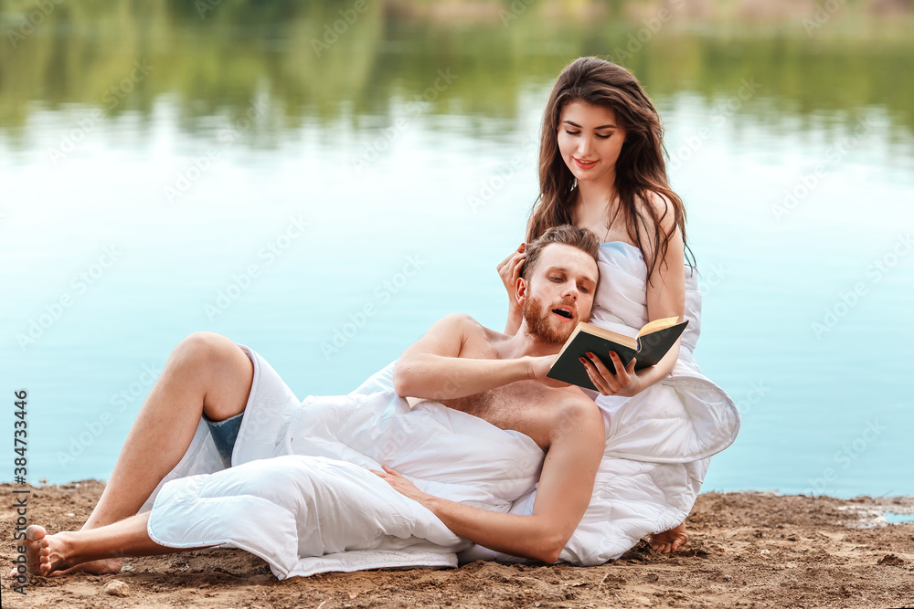 caucasian couple wrapped in a blanket lie on the riverbank and read a book. Self isolation from people. Unity with nature and digital detox