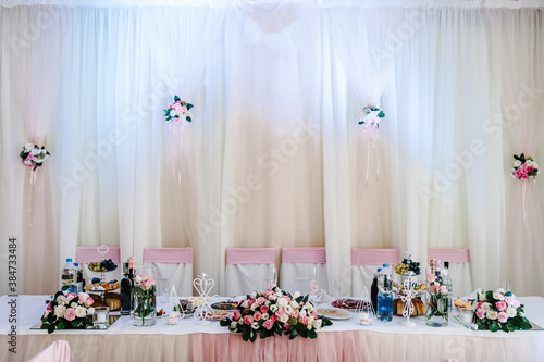 Festive tablen stands decorated with composition of pink flowers and greenery in the banquet hall. Table newlyweds in the banquet area on wedding party. photo