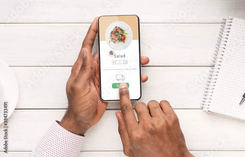 Healthy food at office or home and active lifestyle. Hands of african american man hold smartphone with meal ordering