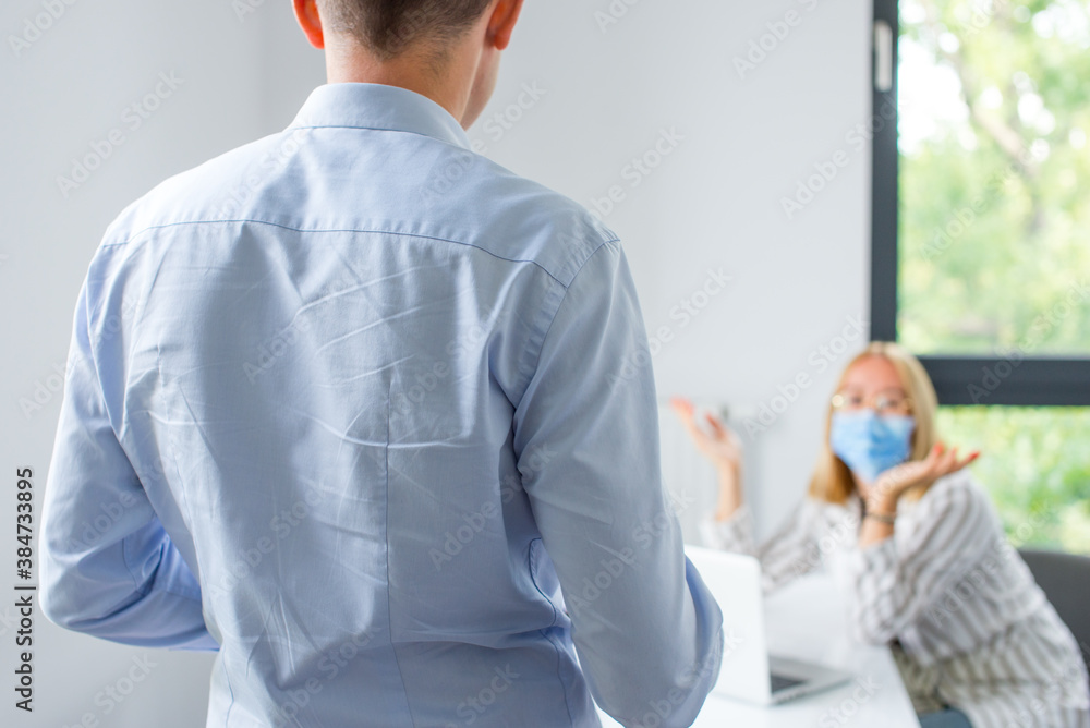 Work in a corporation during a pandemic. The man is giving a presentation and the woman wearing the face mask. Two business colleagues wearing protective face mask on a meeting during coronavirus. Work in a corporation during a pandemic. The man is giving a presentation and the woman wearing the face mask. Two business colleagues wearing protective face mask on a meeting during coronavirus.