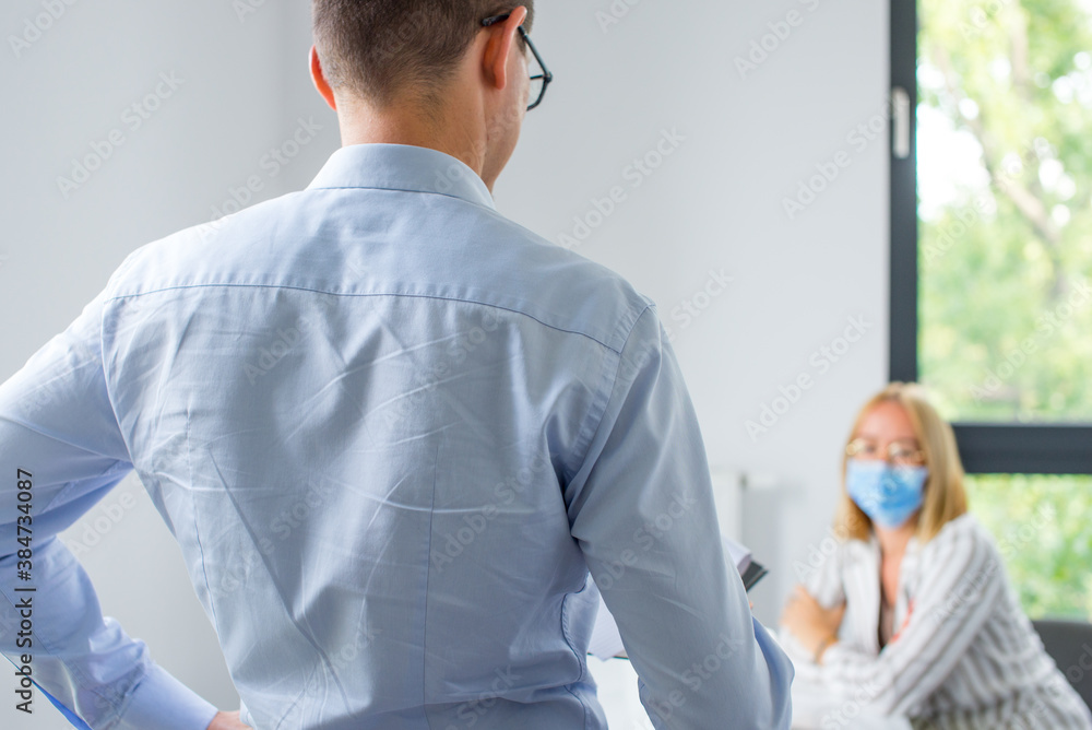 Work in a corporation during a pandemic. The man is giving a presentation and the woman wearing the face mask. Two business colleagues wearing protective face mask on a meeting during coronavirus. Work in a corporation during a pandemic. The man is giving a presentation and the woman wearing the face mask. Two business colleagues wearing protective face mask on a meeting during coronavirus.