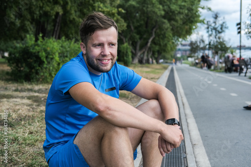 handsome male athlete in blue sportswear looks directly at the camera and smiles after an outdoor workout.