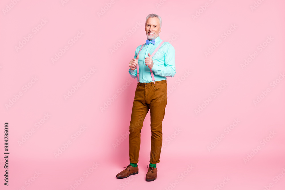 Full length body size portrait of smiling cheerful old gentleman wearing bowtie pants touching suspenders isolated on pink color background Full length body size portrait of smiling cheerful old gentleman wearing bowtie pants touching suspenders isolated on pink color background
