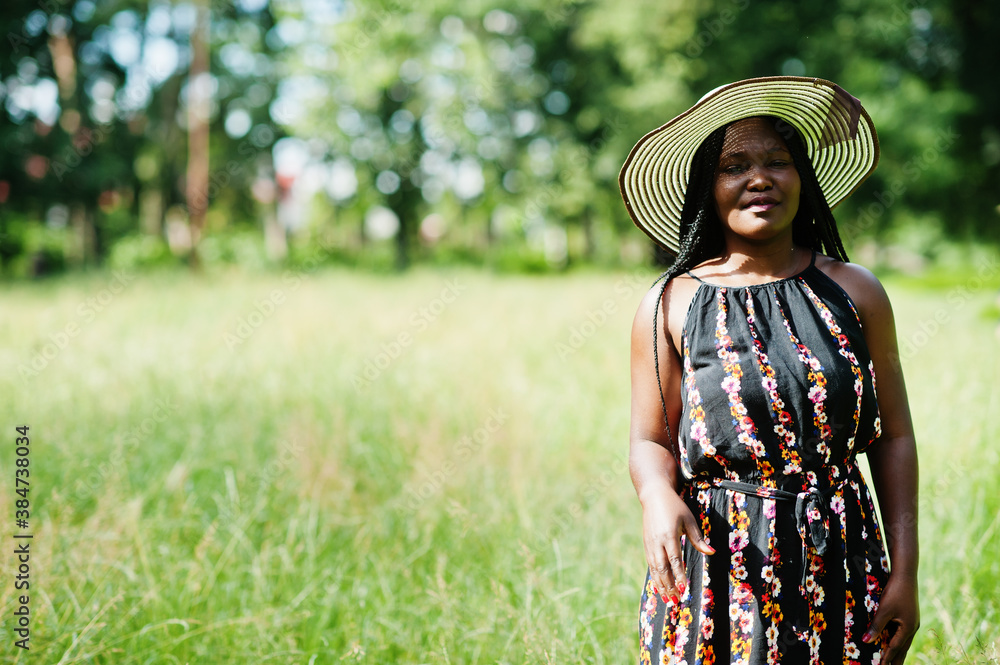 Portrait of gorgeous african american woman 20s in summer hat posing at green grass in park.