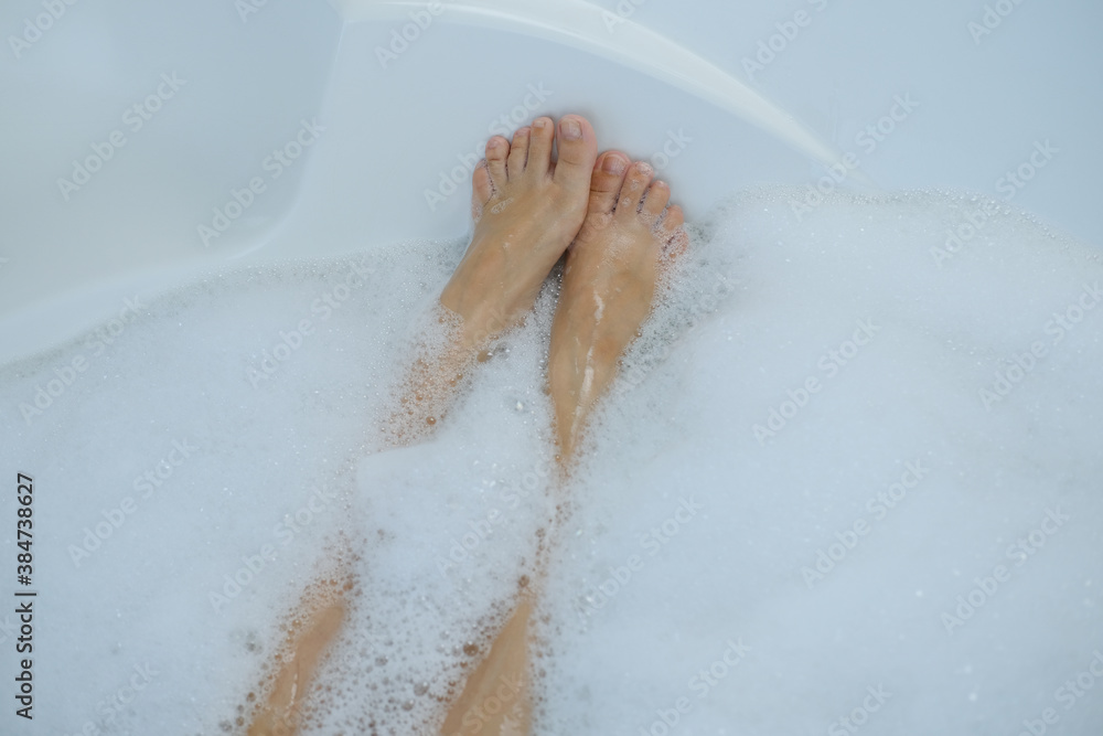 young woman with long legs take a bath at home or hotel, lush white foam, beauty and health concept, daily hygiene