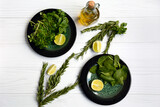 Layout of vegetarian products on two plates with spinach and basil, a bottle of olive oil, rosemary branches and lime