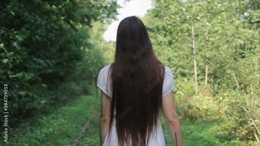 A sensual young woman in a white dress walks along a path among the trees and, turning to the camera throws flowers into the air. Close-up. Slow motion. The camera changes focus A sensual young woman in a white dress walks along a path among the trees and, turning to the camera throws flowers into the air. Close-up. Slow motion. The camera changes focus