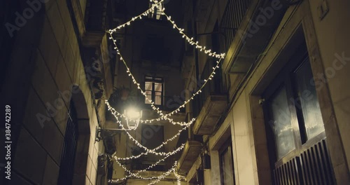 Smooth camera shot along narrow street at the night in the center of Barcelona in christmas holidays. View of old streets of Gotico quarter with christmas lights decorations