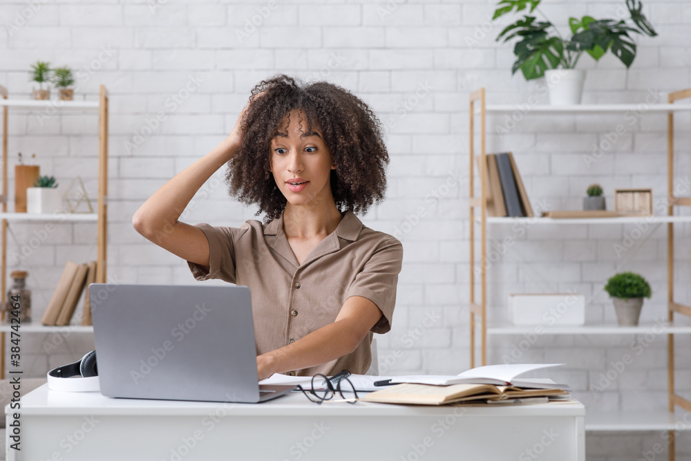 Difficult task or problems at online work. Surprised african american woman scratches her head and looks at laptop Difficult task or problems at online work. Surprised african american woman scratches her head and looks at laptop