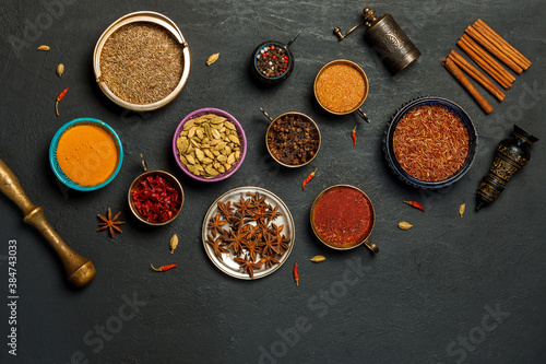 Bright spices and fragrant dried herbs in colored bowls, pepper mill on a black background. Top view, with space. Concept of national cuisine.
