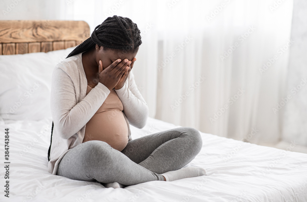 Hormonal changes during pregnancy. Depressed black pregnant lady sitting on bed crying Hormonal changes during pregnancy. Depressed black pregnant lady sitting on bed crying