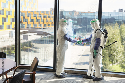 Wallpaper Mural Full length portrait of two disinfection workers wearing hazmat suits shaking hands while standing against window in office, copy space Torontodigital.ca