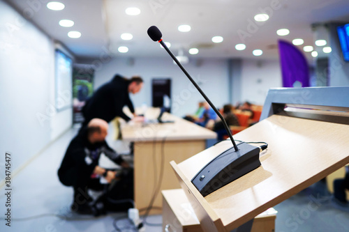 Meeting room microphone. Technical workers are preparing equipment for the conference. Blurred background. Unrecognizable faces.