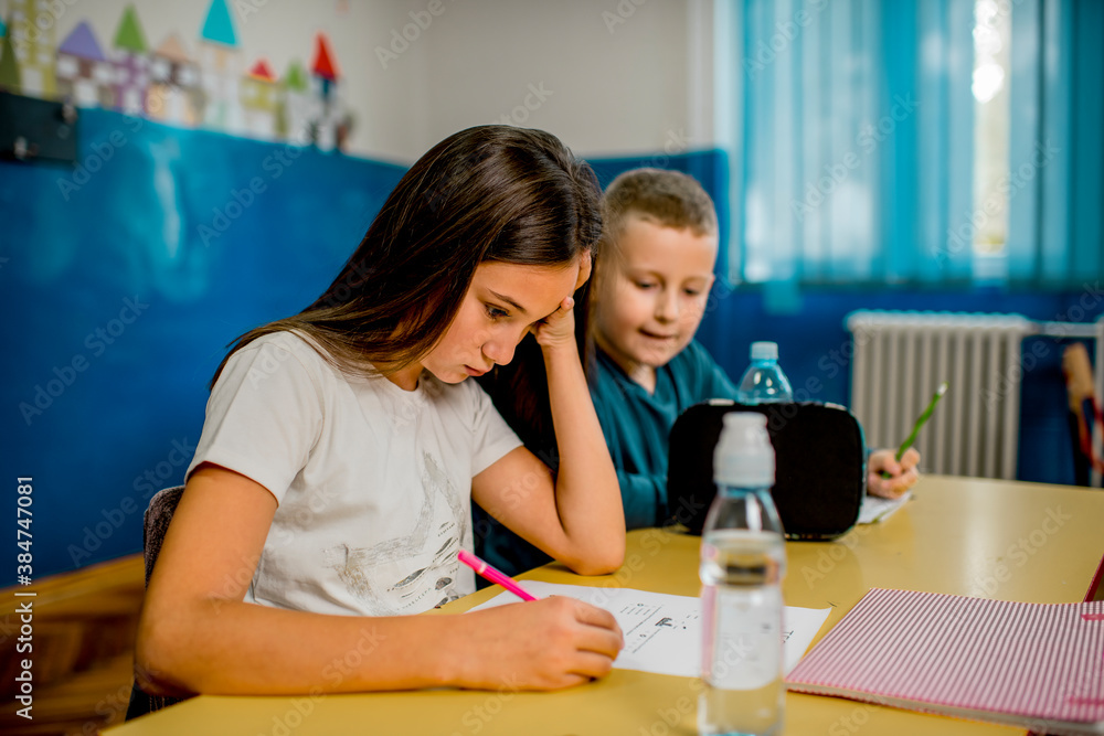 Elementary schoolchildren writing at the desk in the classroom.