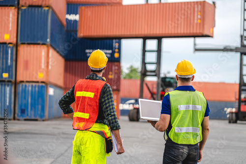 Professional of two engineer container cargo foreman in helmets working standing and using walkie talkie checking stock into container for loading.logistic and business export