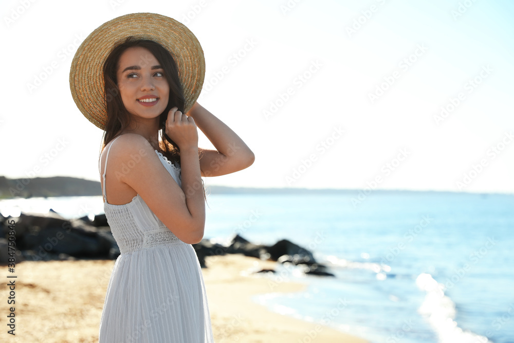 Happy young woman with hat on beach near sea. Space for text