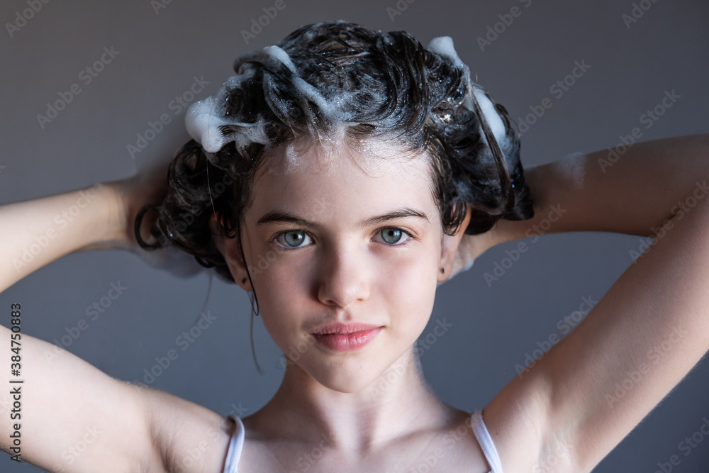 little / young girl washes her hair, soap suds from shampoo on her head, portrait. Child makes horns from hair