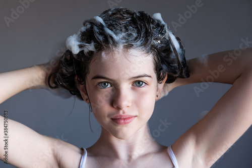 Obraz na płótnie little / young girl washes her hair, soap suds from shampoo on her head, portrait. Child makes horns from hair w salonie