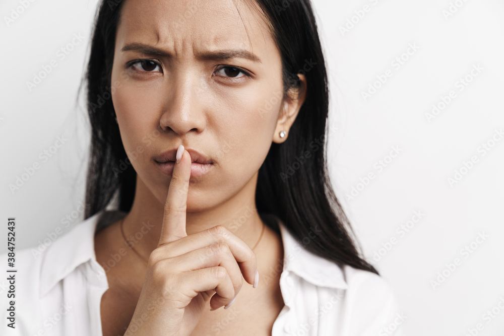 Beautiful displeased asian woman showing silence gesture at camera Beautiful displeased asian woman showing silence gesture at camera