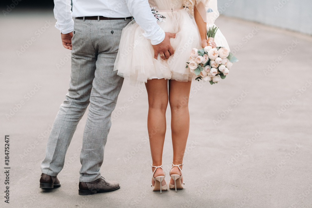 The groom puts his hand on the ass of his bride. The bride in a short dress  back holding a bouquet in her hands Stock-Foto | Adobe Stock