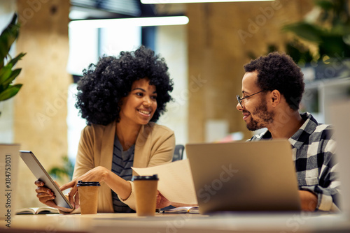 Sharing fresh ideas. Two young happy multiracial business people sitting at desk and communicating while working together in coworking space