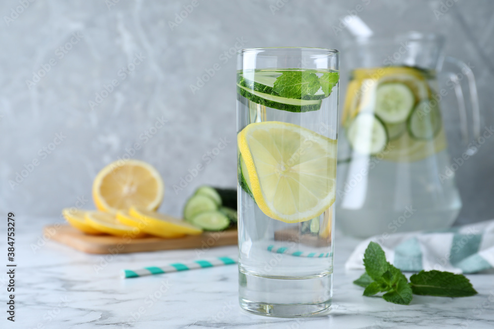 Refreshing water with cucumber, lemon and mint on white marble table. Space for text
