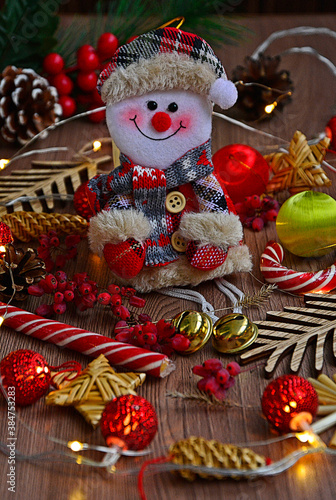 Close-up toy snowman sits among burning garlands on wooden table