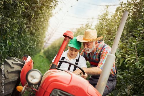 Young boy learns to drive a tractor with the help of his grandfather