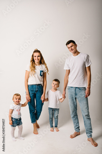 Family portrait of parents and children in denim casual style clothes. Fashion models on white background. Smiling young mother and father with daughter and son posing together.