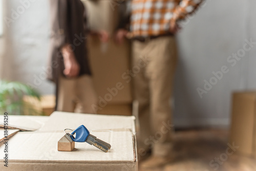 keys lying on cardboard box on foreground and blurred view of senior couple, moving concept