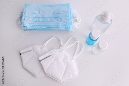 Hand sanitizers and respiratory masks on white background, flat lay. Protective essentials during COVID-19 pandemic