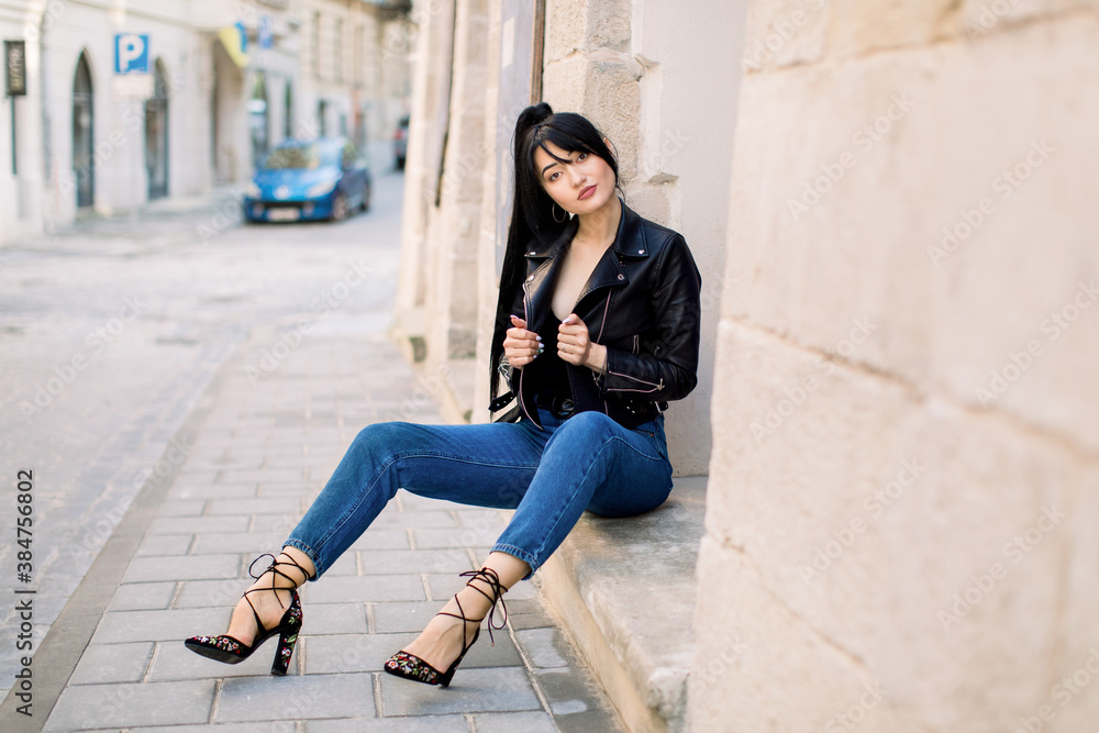City life, people and fashion concept. Sexy young attractive Asian woman, wearing jeans, heels and black leather jacket, posing to camera outdoors in the sity, sitting on the stairs of building City life, people and fashion concept. Sexy young attractive Asian woman, wearing jeans, heels and black leather jacket, posing to camera outdoors in the sity, sitting on the stairs of building