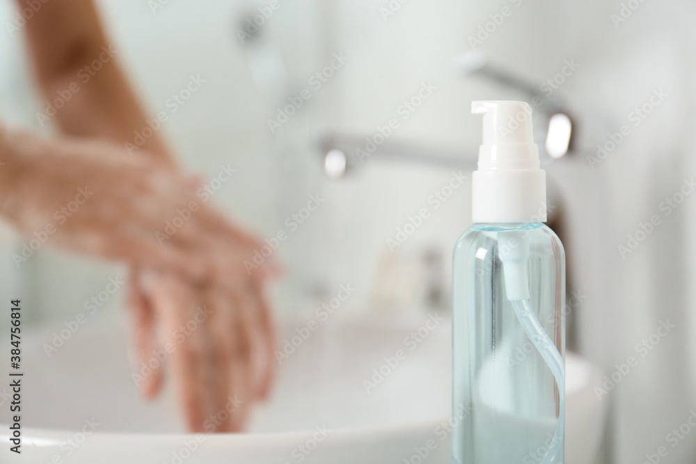 Bottle of antibacterial soap and blurred woman washing hands on background. Personal hygiene during COVID-19 pandemic - obrazy, fototapety, plakaty 