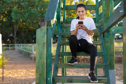 Young beautiful woman wearing sport clothes in the forest very happy and smiling, sitting and chatting on the phone