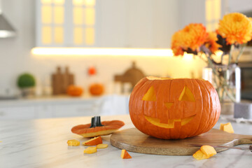 Pumpkin jack o'lantern on white marble table in kitchen, space for text. Halloween celebration