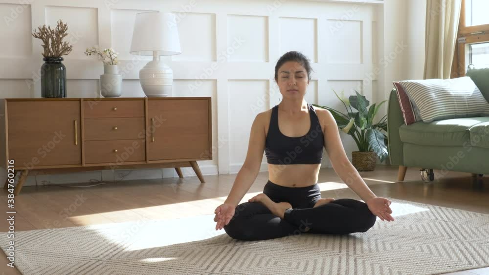 Young Indian Woman Meditating sitting on the Carpet and Inhaling and Exhaling, doing Yoga, Black Sportswear Light Room At home in the Morning. Yoga student doing exercises then relaxing in lotus pose Young Indian Woman Meditating sitting on the Carpet and Inhaling and Exhaling, doing Yoga, Black Sportswear Light Room At home in the Morning. Yoga student doing exercises then relaxing in lotus pose