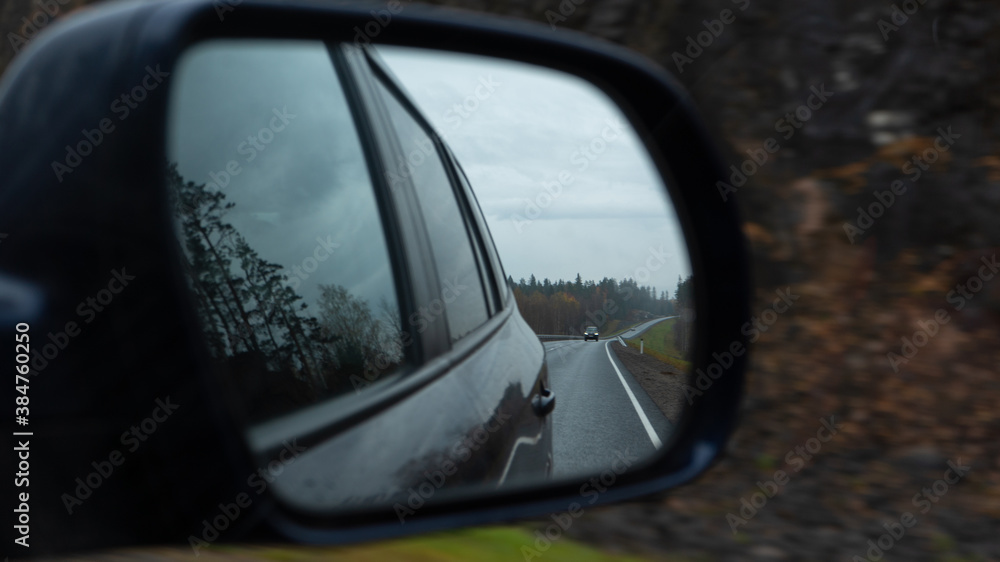the car drives along the road at dusk and the road, nature and other car are reflected in the rearview mirror