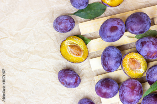 Top view of fresh raw blue and violet plums with green leaves on light wooden background with copy space.