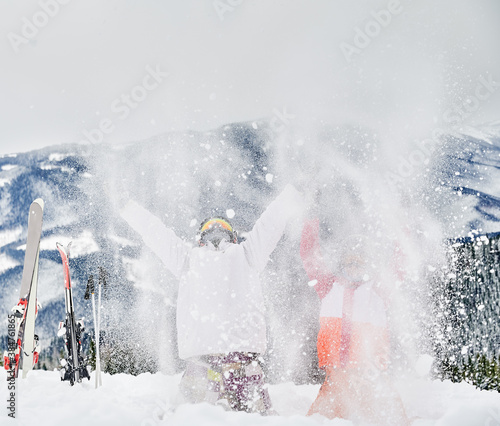 Two skiers throwing fresh powder snow high in the air. Man and woman having fun at ski resort with beautiful mountains on background. Concept of winter sport activities, fun and relationships.