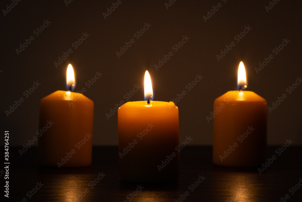 Three lit candles burning in the darkness. Golden tones with selective focus and background blur Three lit candles burning in the darkness. Golden tones with selective focus and background blur
