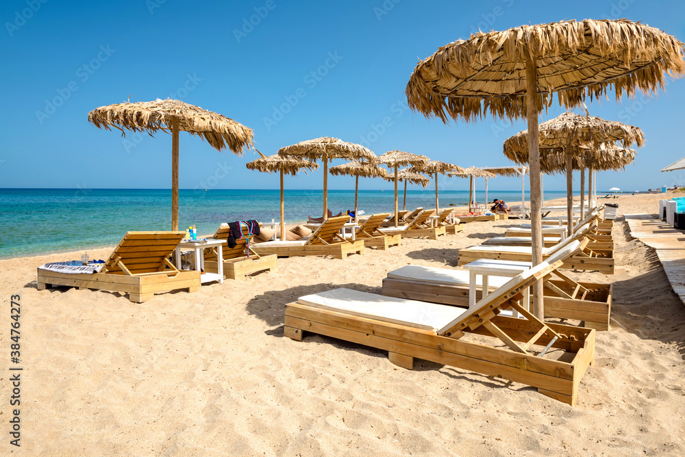 Orginized sandy beach during summer time, with wooden sun beds and straw umbrellas 