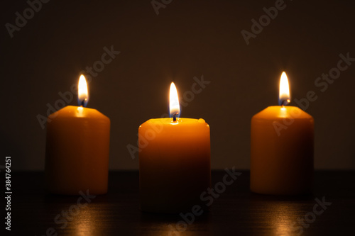 Three lit candles burning in the darkness. Golden tones with selective focus and background blur