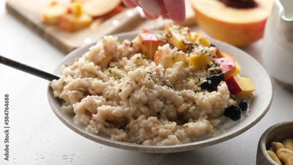 Adding hemp seeds to oatmeal porridge bowl. Healthy vegan breakfast food Adding hemp seeds to oatmeal porridge bowl. Healthy vegan breakfast food