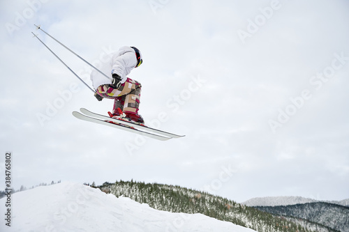 Horizontal snapshot of spectacular freeriding fly at the steep slopes by skier. Cool ski jump from hill against cloudy sky on background. Low angle view, copy space. Extreme sport concept