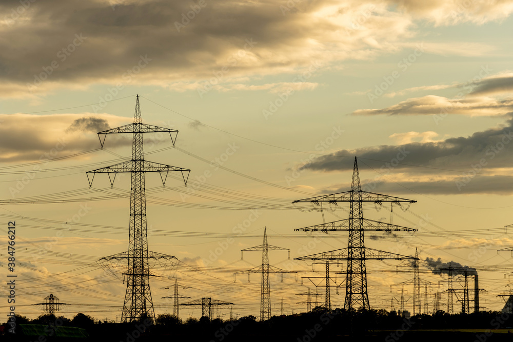 Fototapeta premium Hochspannungsmasten als Silhouetten in der Abenddämmerung , Energieverbindung vom Kraftwerk zum Verbraucher.