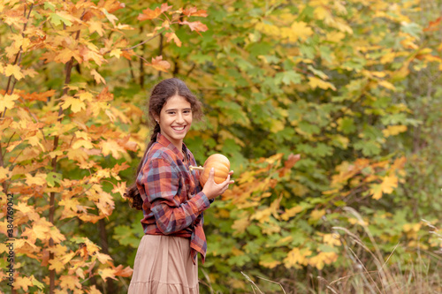 Portrait of beautiful cheerful girl with a pumpkin on a background of autumn trees celebrating happy Thanksgiving day.
