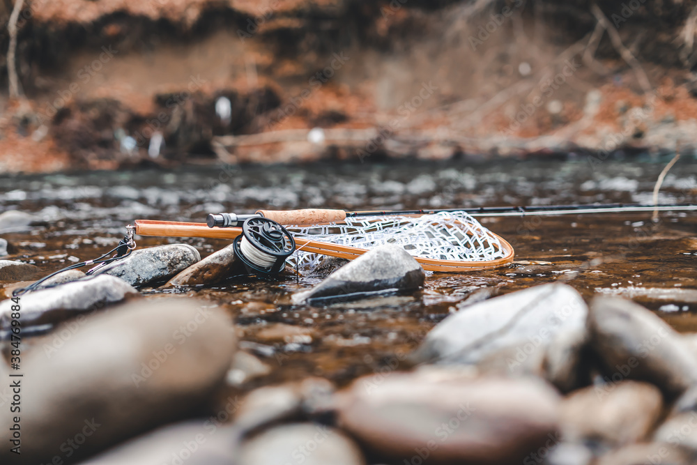 Fly fishing gear on rocks near water. Reel, rod and landing net Fly fishing gear on rocks near water. Reel, rod and landing net