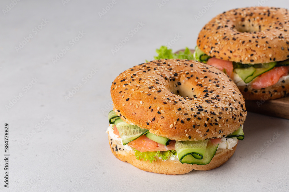 Bagel with smoked salmon, cream cheese, salad and cucumber. Light pink background. Copy space.
