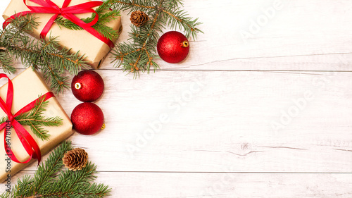 Merry Christmas frame and wallpaper. Happy New Year composition. Christmas gift, red balls, pine cones, fir branches on wooden white background